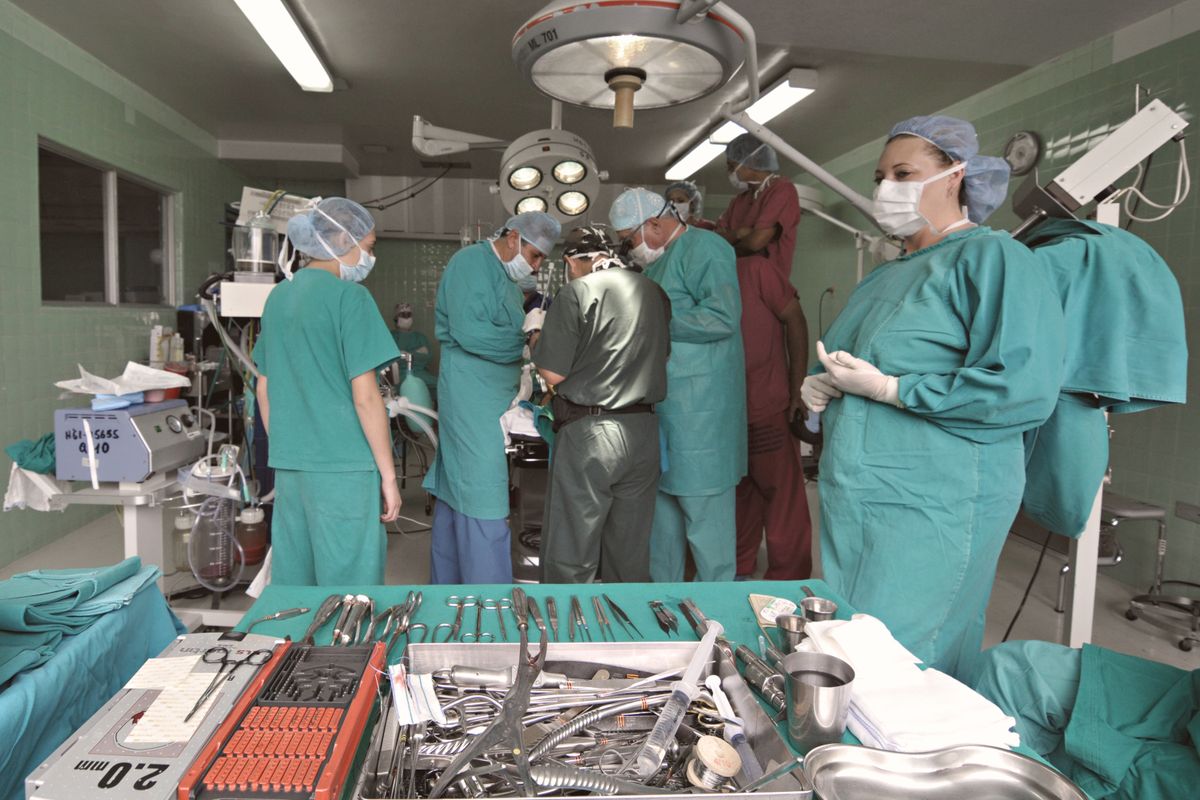 Equipe médica em centro cirúrgico durante procedimento, com instrumentais organizados sobre a mesa